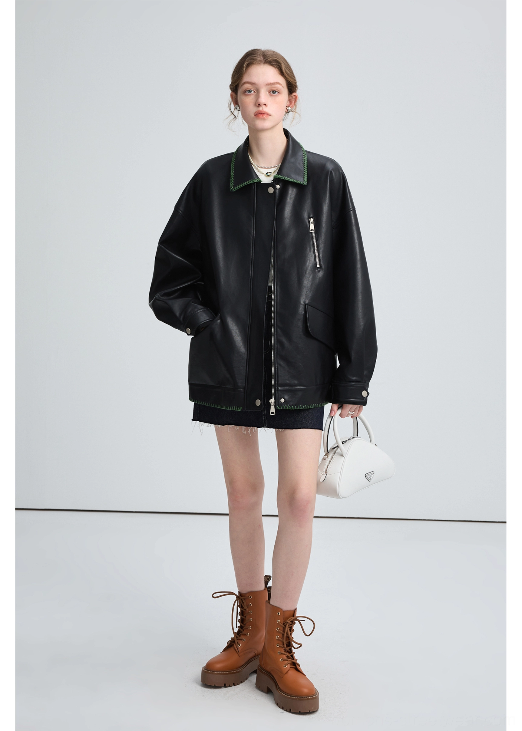 Woman wearing a relaxed black PU leather biker jacket with snap hem, zippered chest pocket, denim skirt, and brown boots