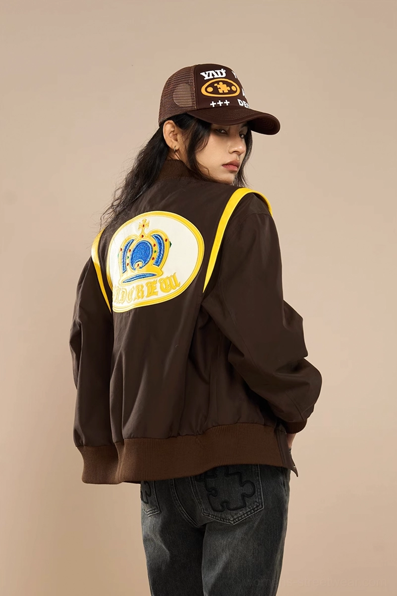 Female model wearing relaxed brown embroidered bomber baseball jacket with dark jeans and trucker cap