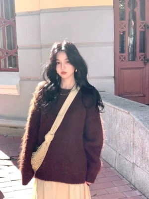 Warm coffee-toned fuzzy knit sweater with relaxed deep-V neckline and long sleeves styled with an apricot midi skirt and mesh crossbody bag on a European-inspired street