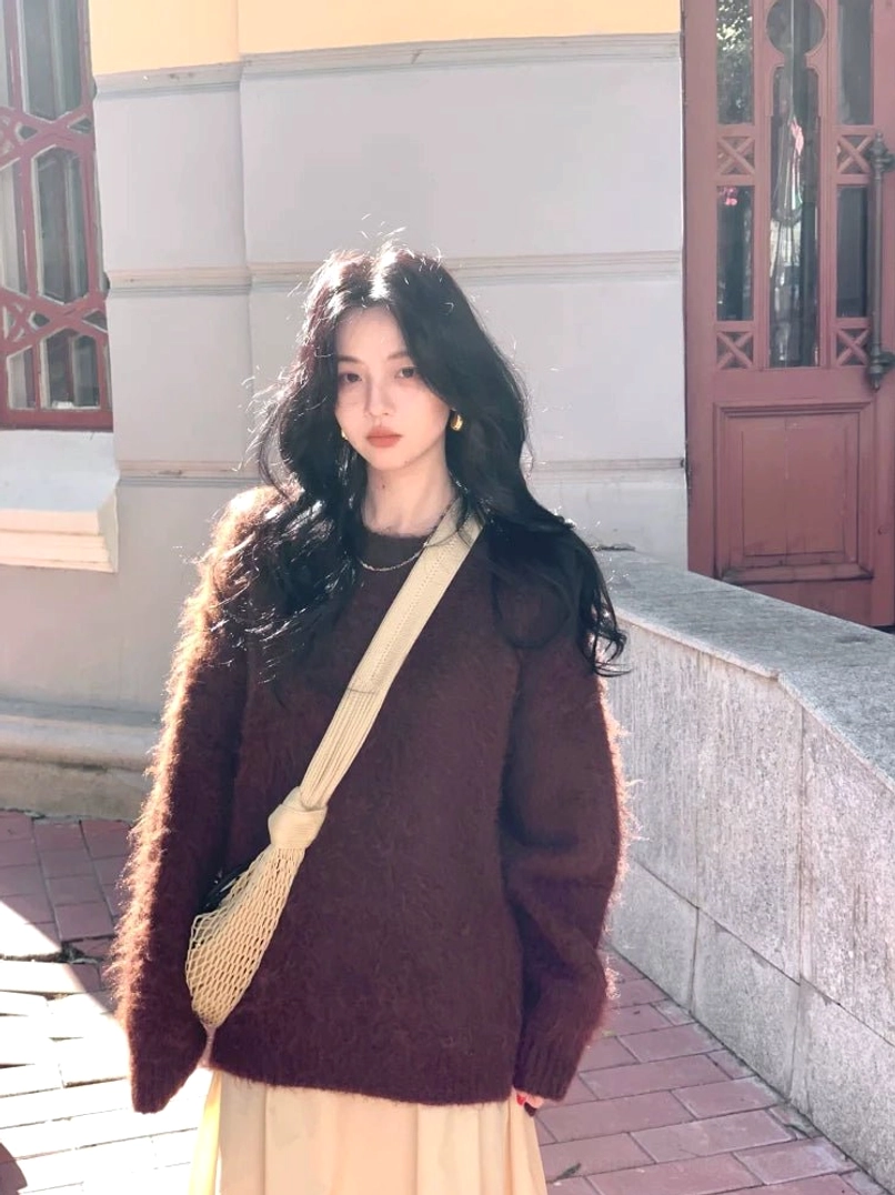 Warm coffee-toned fuzzy knit sweater with relaxed deep-V neckline and long sleeves styled with an apricot midi skirt and mesh crossbody bag on a European-inspired street