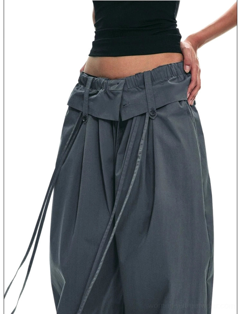 Dark gray paperbag wide-leg streetwear trousers close-up showing adjustable drawstring waistband vertical pleats and smooth woven fabric