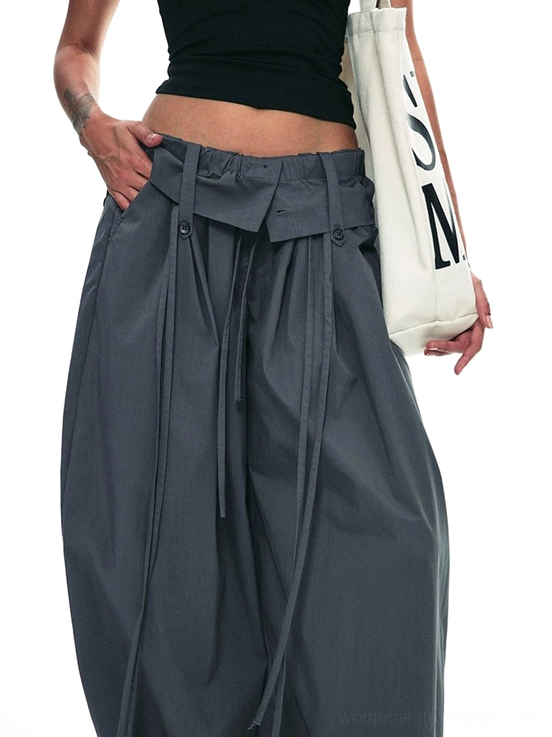 Close-up of dark gray paperbag trousers with fold-over elastic drawstring waistband front pleats and side pocket detail