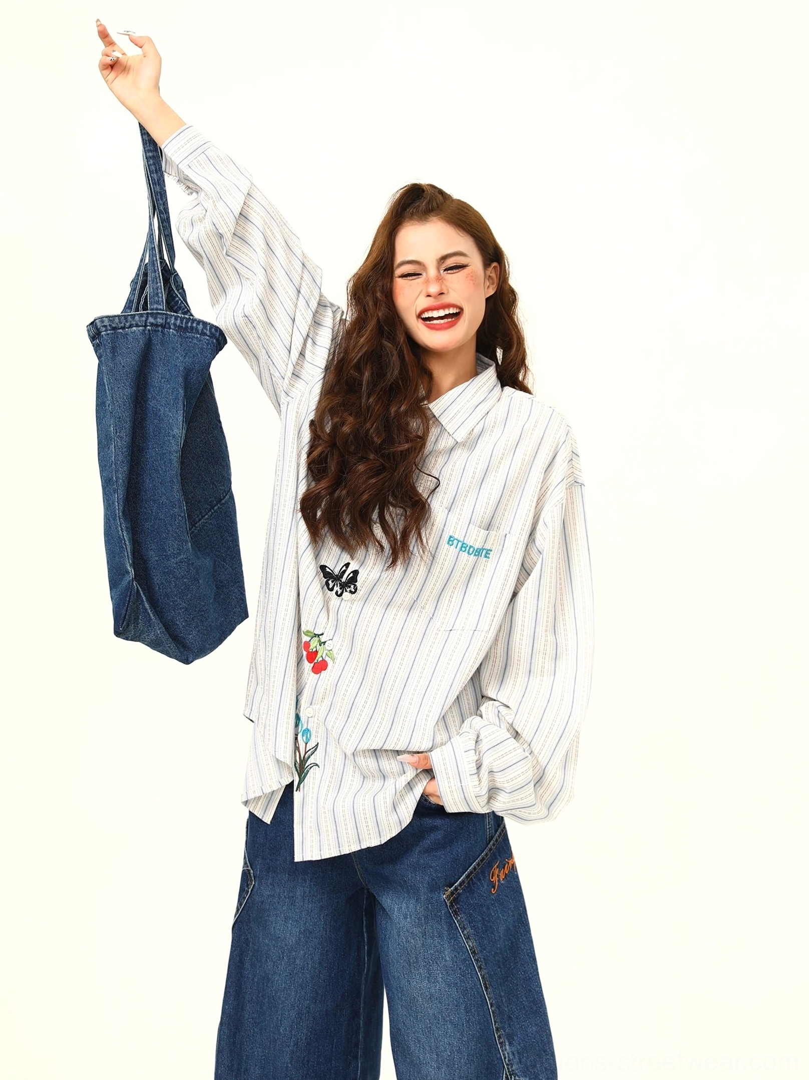 Three-quarter view of a relaxed oversized embroidered striped shirt with playful motifs styled with wide-leg jeans and a denim tote bag