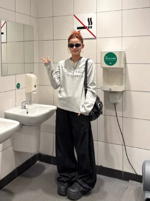 Full-body side view of a woman styling a relaxed grey Henley streetwear top with black wide-leg jeans platform shoes and shoulder bag