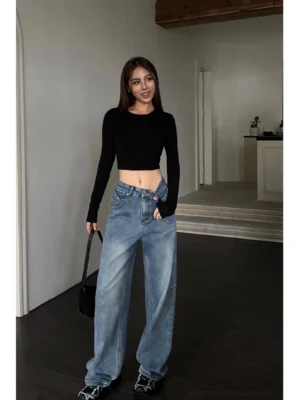 Full-body indoor view of relaxed high-waist wide-leg blue denim jeans styled with a black cropped long-sleeve top