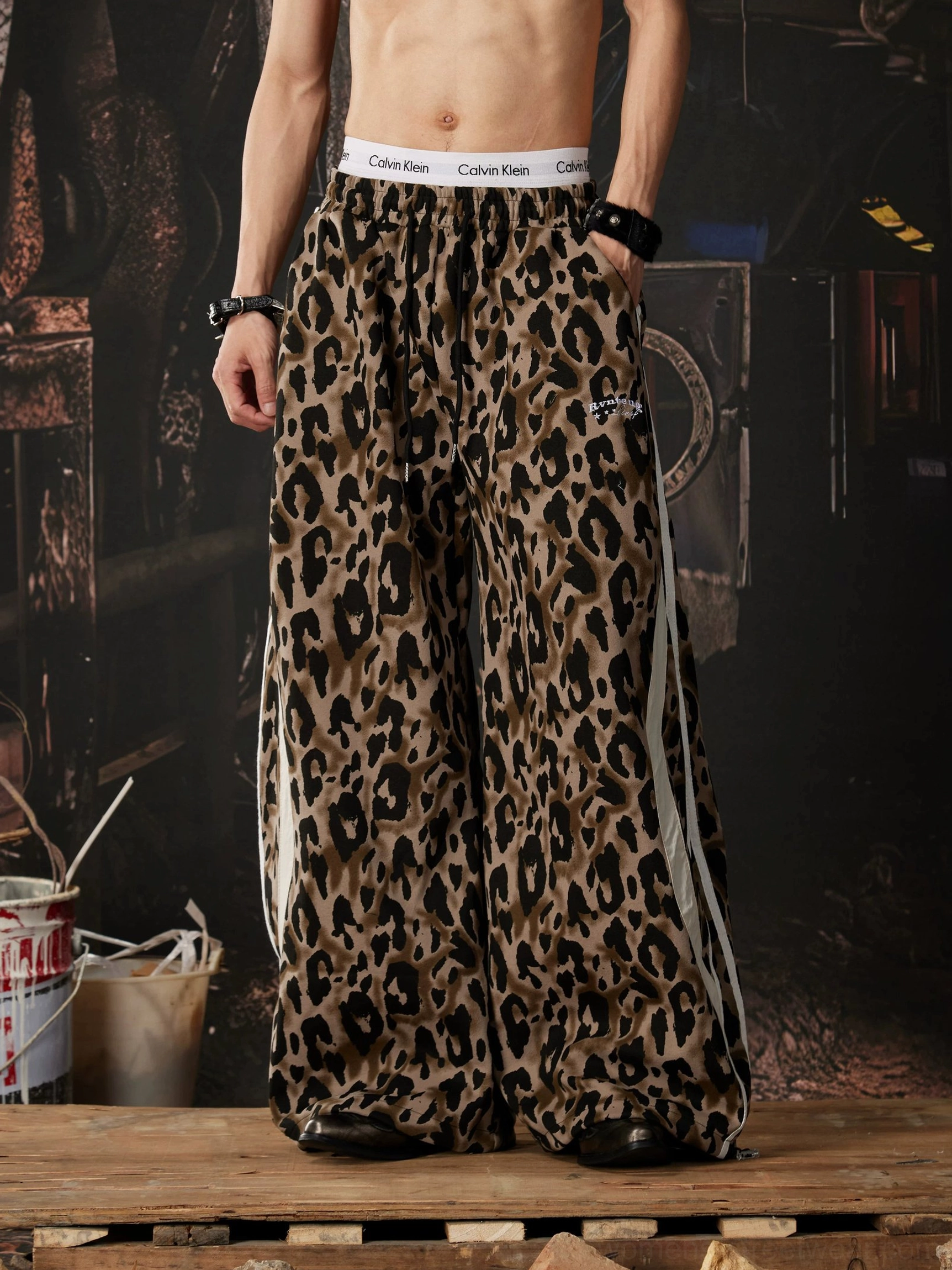 Front standing view of relaxed leopard print streetwear pants with long white side stripe and wide draped legs