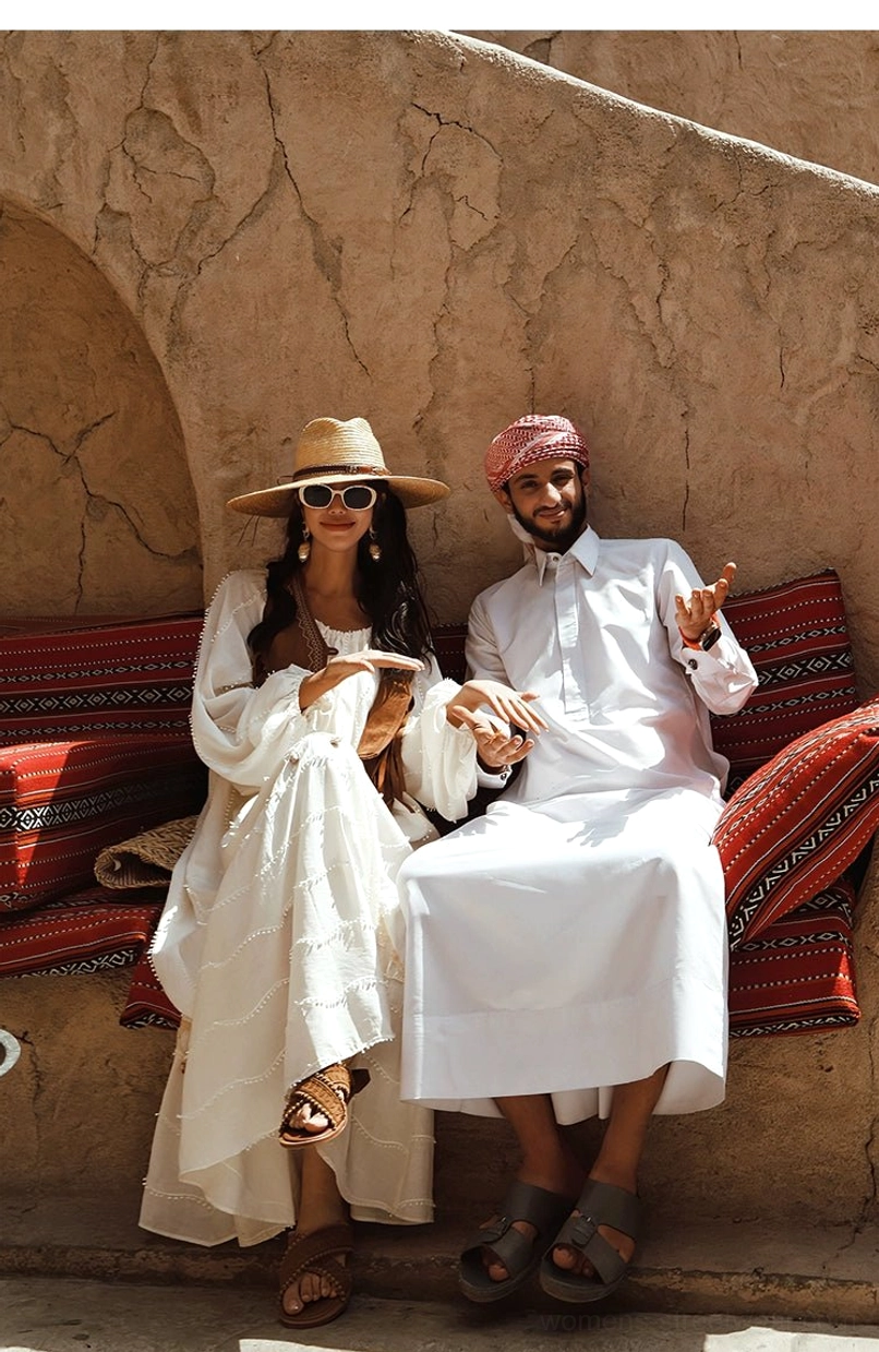 Full-body seated view of a relaxed off-white bohemian maxi dress with long sleeves styled with sunglasses and a straw hat