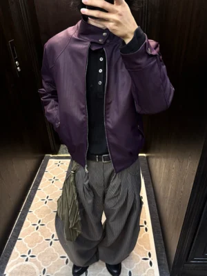 Front view of relaxed pinstripe barrel leg trousers styled with a purple stand collar leather jacket, black waist belt, and draped olive scarf accent