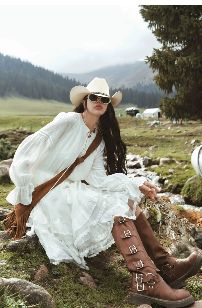 Relaxed white western ruffle midi dress with flowing fabric and tie neckline shown in a seated outdoor grassland look