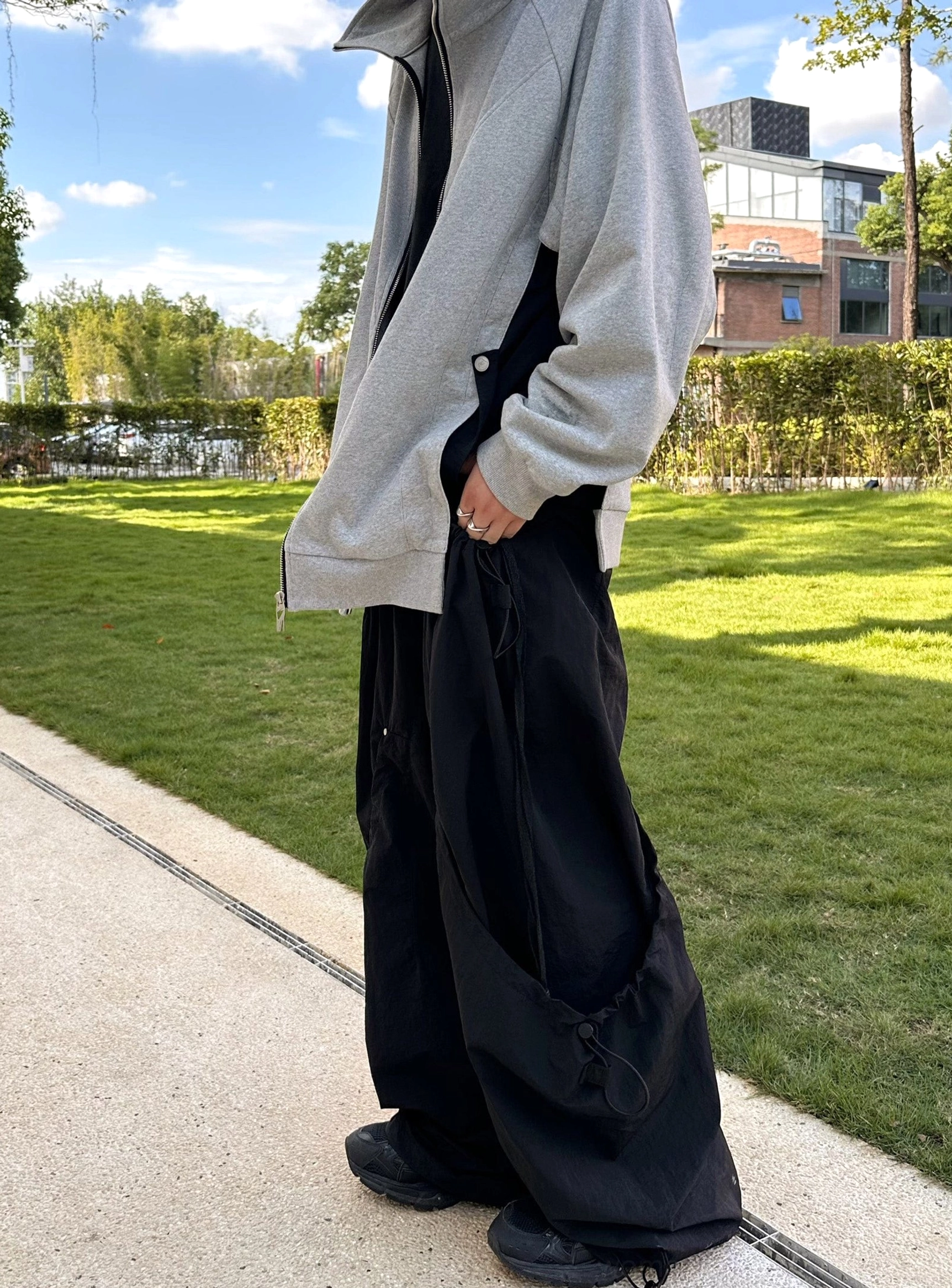 Side view urban outfit featuring relaxed wide leg technical pants and grey zip up jacket on a city park sidewalk