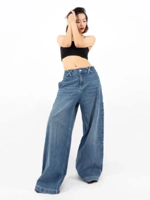 Female model wearing retro blue wide-leg denim jeans with a black cropped tank top in a front full-body studio view