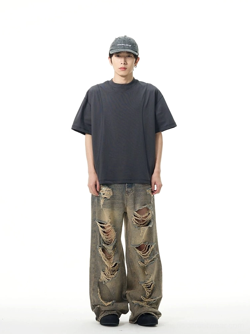 Full front view of oversized retro blue wide-leg ripped jeans on a model wearing a baseball cap and dark casual t-shirt