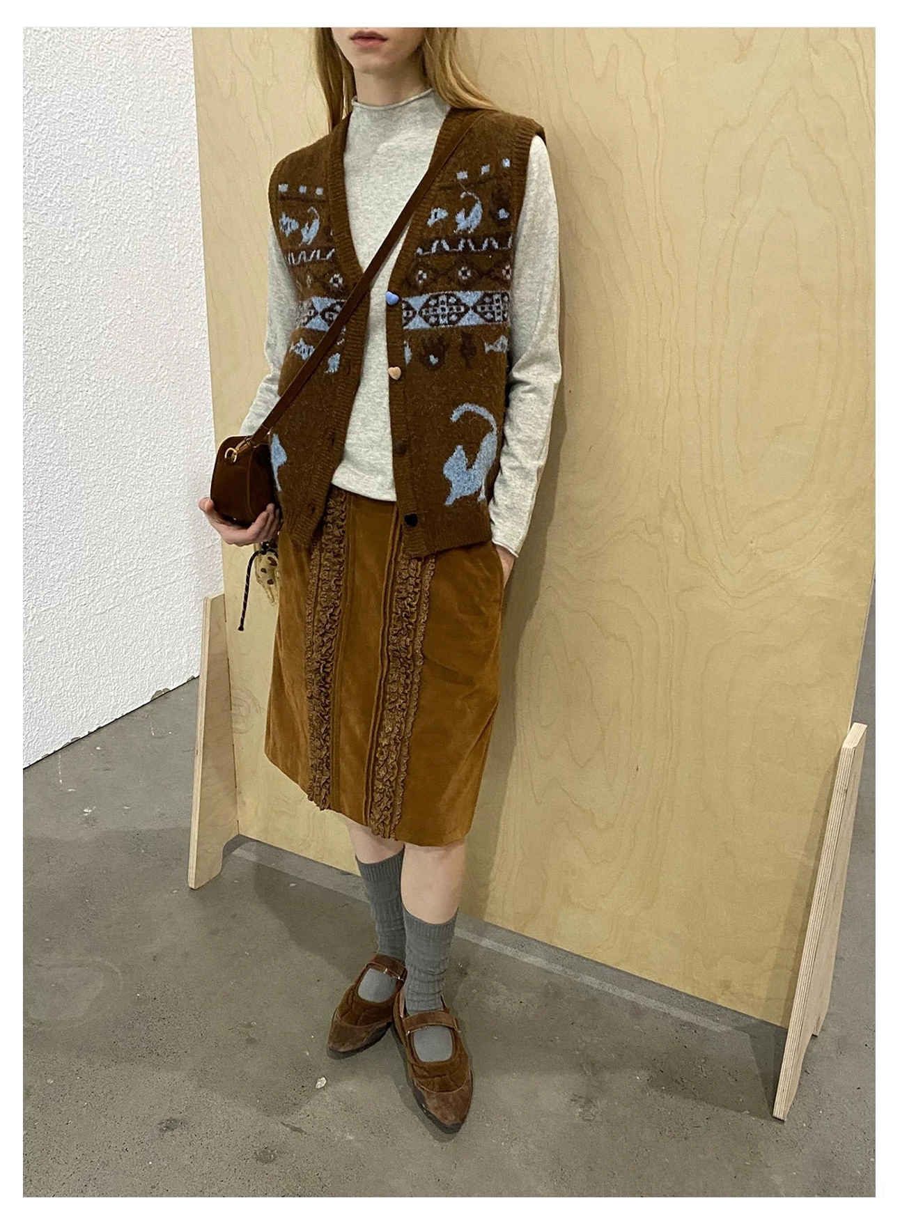 Side view of a retro brown corduroy midi skirt with lace trim styled in layered vintage streetwear against a wooden studio background