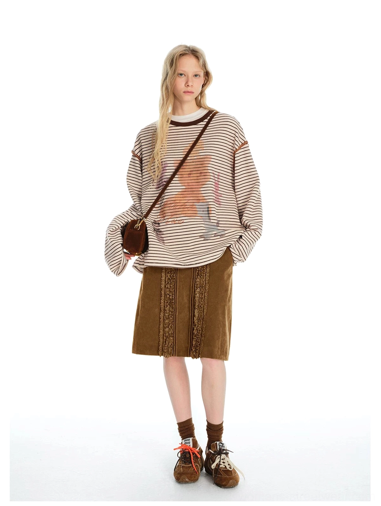 Front view of a retro brown lace trim midi skirt styled with a striped graphic sweater crossbody bag and retro sneakers