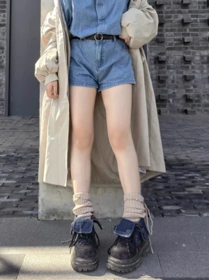 Model wearing retro denim cuff platform ankle boots with denim shorts, slouch socks, and trench coat on brick pavement