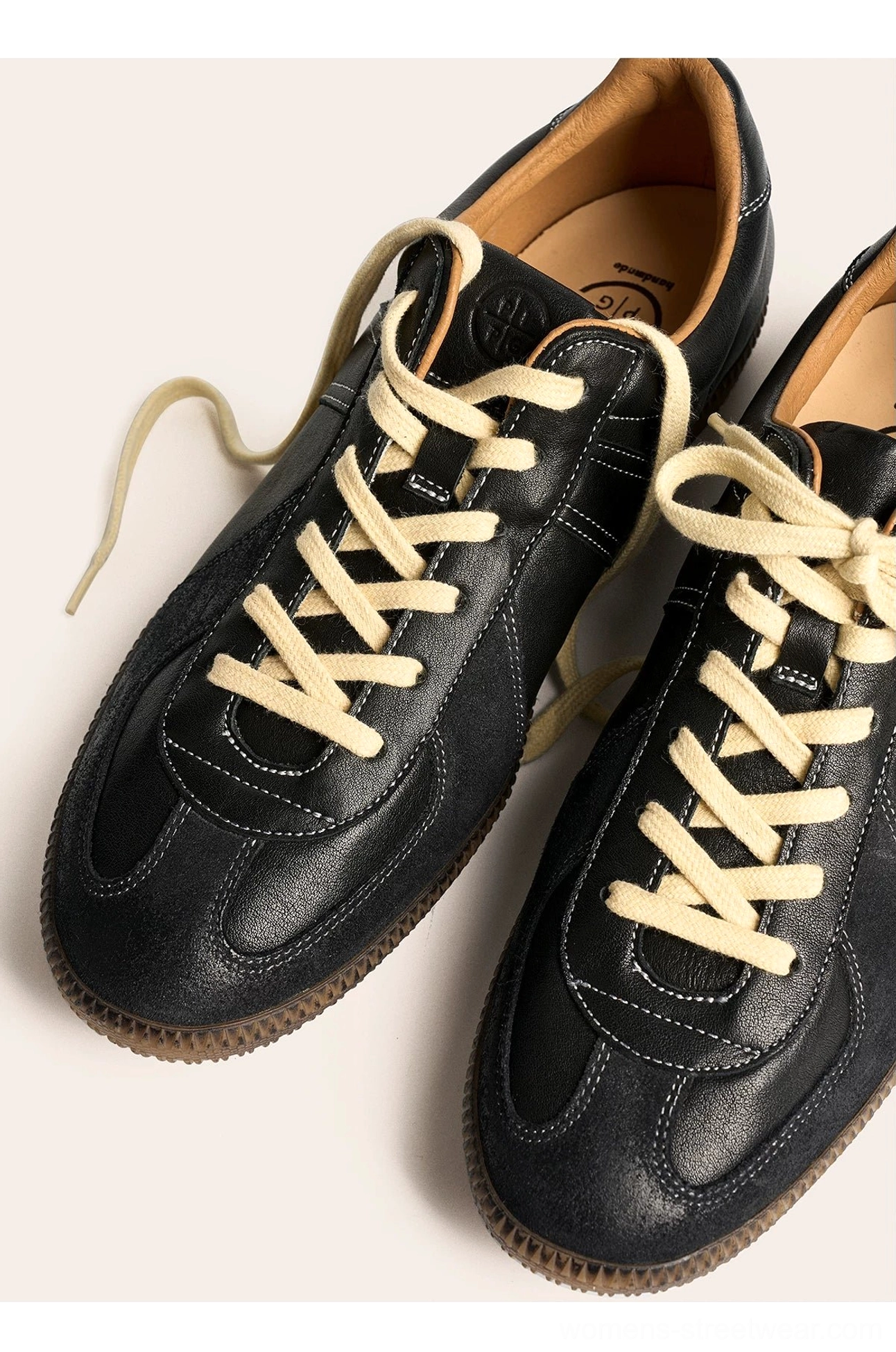Close overhead view of black retro leather sneakers with loosely tied cream laces, suede accents, and gum soles