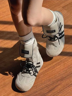 Top view of off-white and black high-top boxing trainer boots styled with letter print crew socks on a wooden floor
