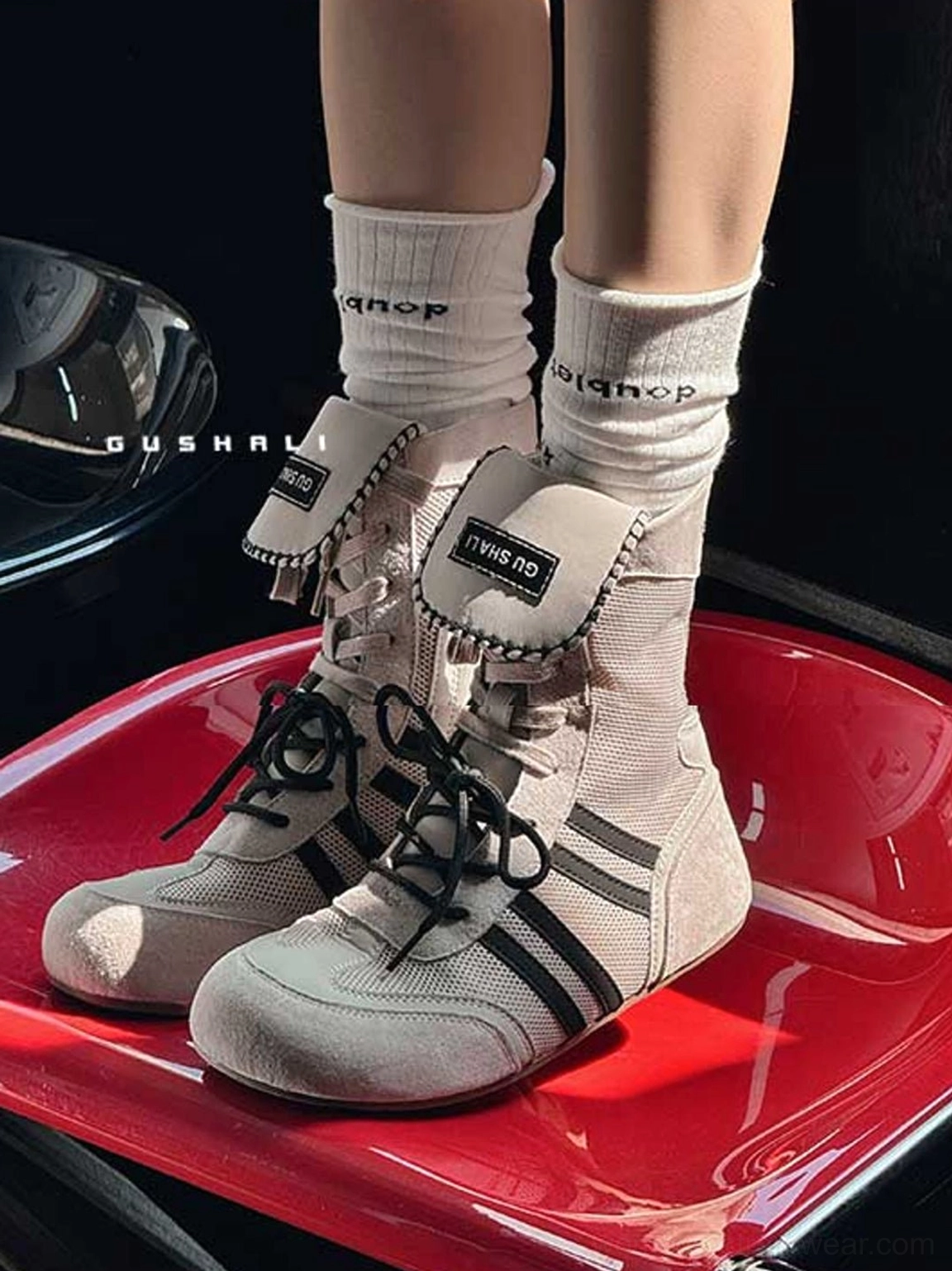Close-up of off-white retro boxing trainer boots with black stripe details worn with printed crew socks against red seating