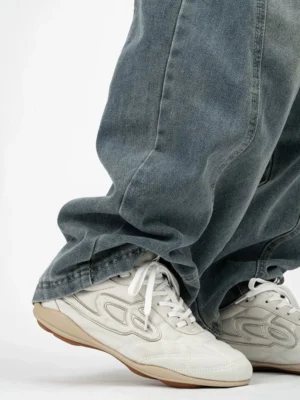 Retro low-top sneaker shown from the rear side while worn with washed blue jeans, highlighting the streamlined training shoe silhouette and casual streetwear proportions