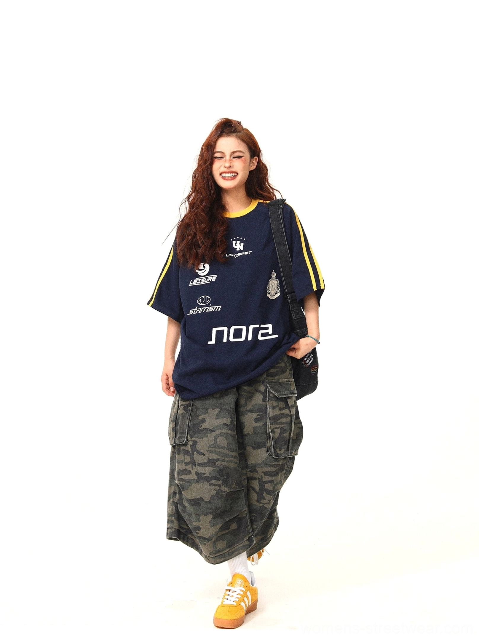 Retro navy varsity graphic oversized tee styled with camo cargo pants yellow sneakers and crossbody bag walking view