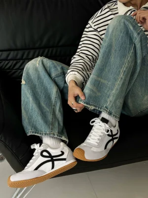 Male model wearing retro panel gum sole streetwear sneakers with white crew socks and ripped jeans while seated indoors