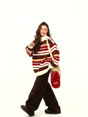 Woman wearing a retro multicolor striped oversized knit zip-up sweater with dark brown wide-leg pants, canvas bag, and red baseball cap in a streetwear studio outfit