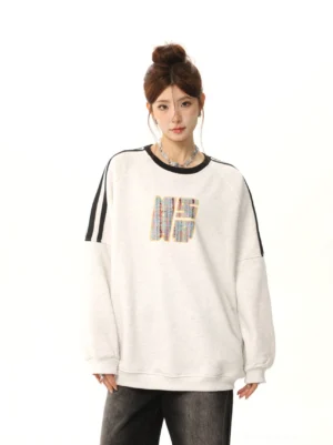 Female model wearing a beige gray fleece retro three-stripe embroidered oversized crewneck sweatshirt with black ribbed trim and dark wide-leg jeans front full-body studio view