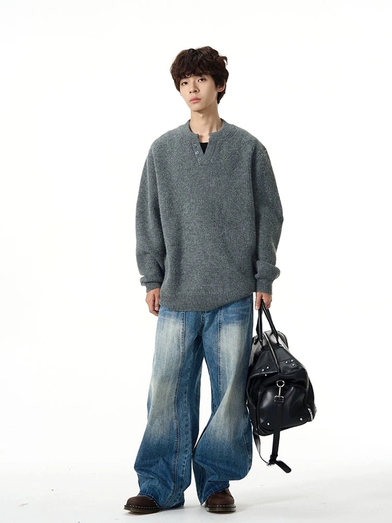 Front view of relaxed faded blue wide-leg jeans styled with a grey oversized V-neck sweater and black leather travel bag