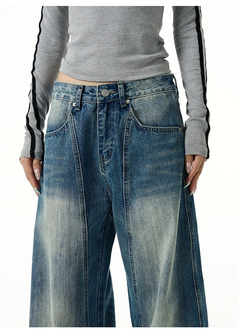 Close-up of faded blue wide-leg jeans showing the button and zip fly, front slant pockets, and central front seam
