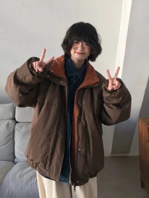 Brown side of reversible oversized padded streetwear jacket styled with a denim shirt and beige loose trousers in a minimalist studio