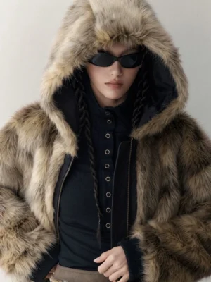 Close-up portrait of a model wearing the plush beige brown faux fur side of a reversible hooded winter streetwear jacket with the hood up