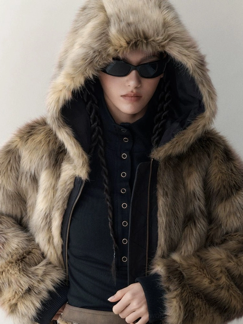 Close-up portrait of a model wearing the plush beige brown faux fur side of a reversible hooded winter streetwear jacket with the hood up