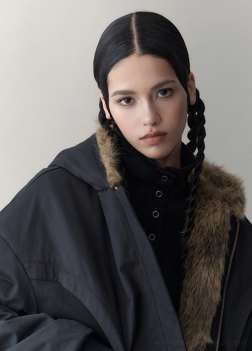 Close-up of the black outer side of a reversible hooded faux fur jacket showing the warm brown fur-lined hood and front fastening
