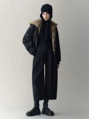 Model wearing the black shell side of an oversized reversible hooded faux fur winter jacket with brown faux fur collar in a minimalist streetwear studio