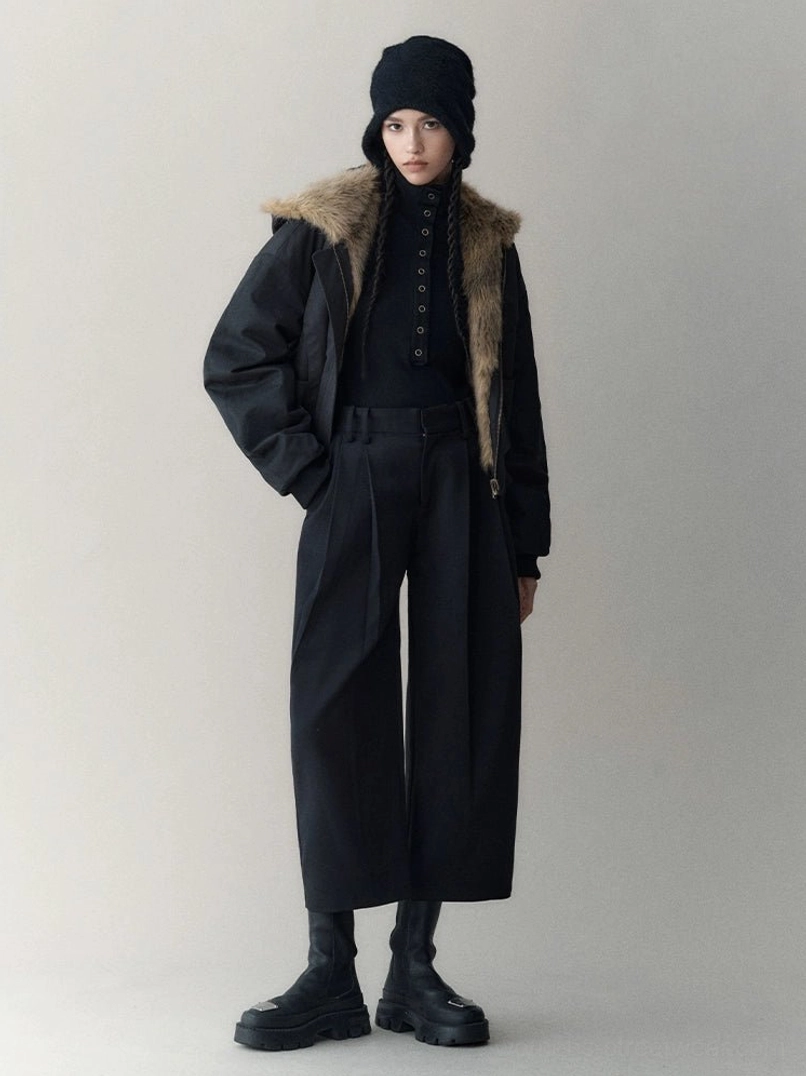 Model wearing the black shell side of an oversized reversible hooded faux fur winter jacket with brown faux fur collar in a minimalist streetwear studio