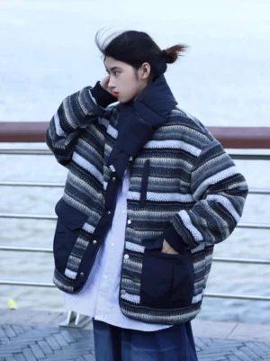 Female model wearing a reversible navy grey striped quilted streetwear coat with detachable padded scarf and black patch pockets by a riverside railing