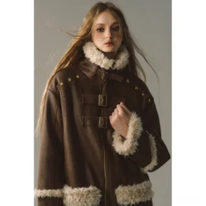 Close-up of reversible suede shearling jacket collar and front closure with cream trim, metal studs, zipper, and vintage buckle hardware