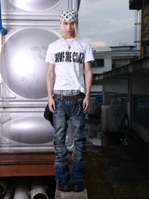 Front view of ripple washed scimitar flare denim pants styled with a graphic T-shirt and leather belt in an industrial streetwear setting