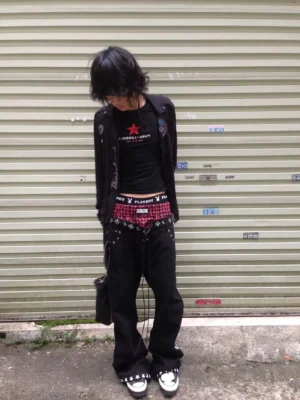 Front view of rocker style black wide leg denim jeans with red checkered waistband, lace-up front, and metal eyelet details