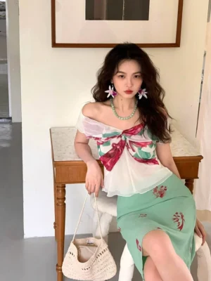 Front view of romantic white floral bow off-shoulder peplum blouse styled with a mint floral midi skirt in a vintage-inspired interior