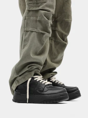 Black chunky platform streetwear sneakers styled with olive green cargo pants and relaxed hanging rope laces in a low angle outfit view