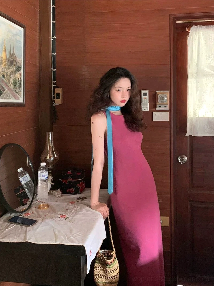Rose red sleeveless side slit slim maxi dress styled with a blue neck scarf and woven handbag in a vintage interior
