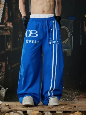 Royal blue oversized Astro Stripe track pants with white side stripes, varsity graphics, wide-leg Korean streetwear silhouette, and elastic waistband