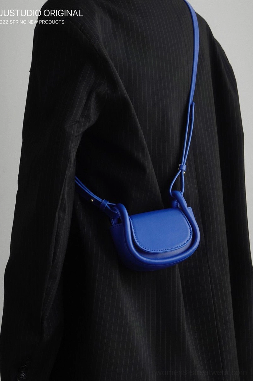 Royal blue mini saddle crossbody bag styled with a black striped suit in a side view