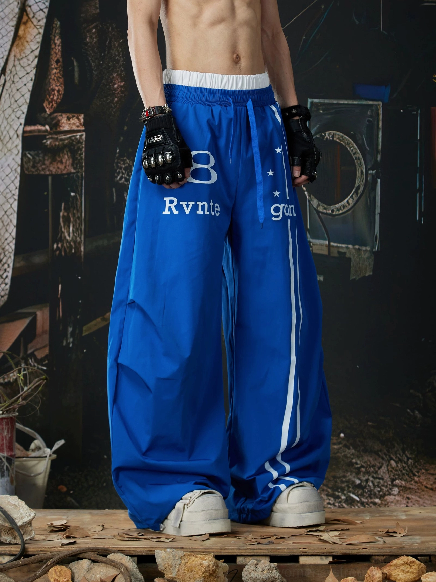 Royal blue wide-leg streetwear track pants shown from a three-quarter angle with white racing stripe and oversized relaxed fit