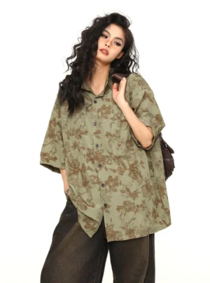 Three-quarter view of a woman wearing an oversized sage green floral button-down shirt with chest pocket and brown crossbody bag