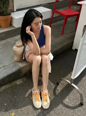 Model wearing sage green and orange lace suede skate shoes with white shorts in an outdoor cafe streetwear outfit