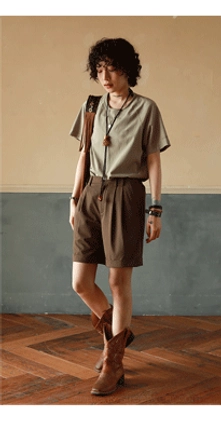 Muted sage green raglan crew neck t-shirt side view showing shoulder construction, styled with brown shorts and cowboy boots