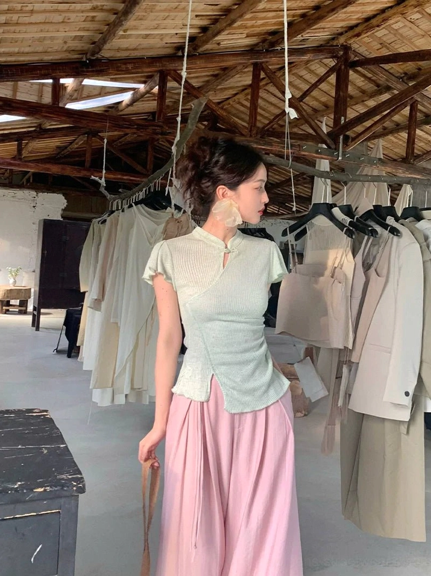 Back three-quarter view showing the fitted silhouette and asymmetric side hem of a sage green ribbed cheongsam top styled with a pink maxi skirt