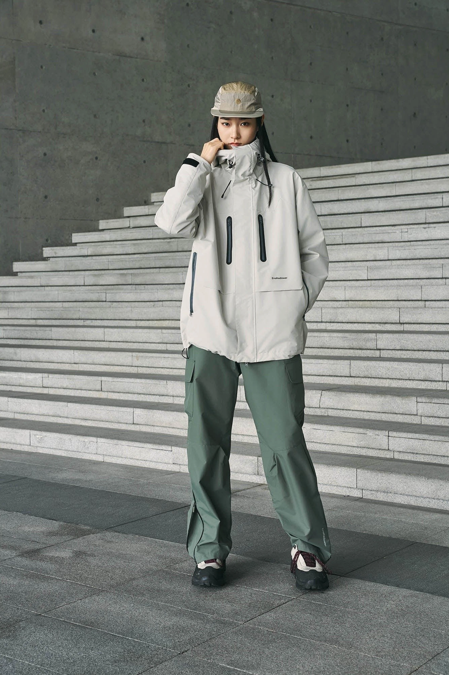 Sage green streetwear cargo pants styled with a light grey outdoor jacket, bucket hat, and casual shoes in an urban outdoor outfit
